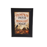 A framed autumn-themed art print with the text 'Pumpkin Patch Moonlight Magic' in orange and black lettering, featuring pumpkins, crows, and a haunted house scene, displayed in a black frame on a light beige background.